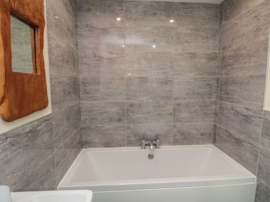 A bathroom with a bathtub tiled walls and a wooden framed mirror at Greenlee House in Seahouses