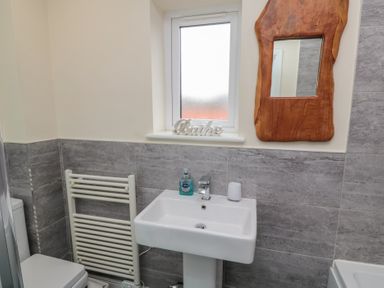 A bathroom with a sink a towel rail a window and a wood framed mirror at Greenlee House in Seahouses