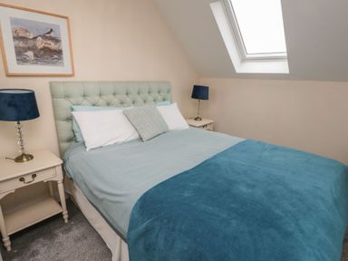 A bedroom with a bed with blue bedding two bedside tables with lamps and a skylight window at Greenlee House in Seahouses
