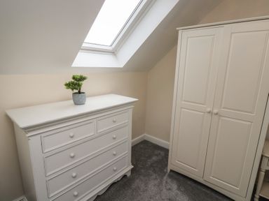 A room with a white chest of drawers with a small plant on top and a white wardrobe under a skylight window at Greenlee House in Seahouses