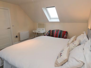 A bedroom with a large bed a skylight window a white dressing table a stool and a patterned armchair at Greenlee House in Seahouses
