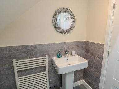 A bathroom with a pedestal sink a decorative round mirror a hand towel radiator and soap dispenser at Greenlee House in Seahouses