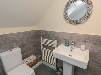 A bathroom with a toilet a sink a round decorative mirror and a wicker basket with toilet paper at Greenlee House in Seahouses