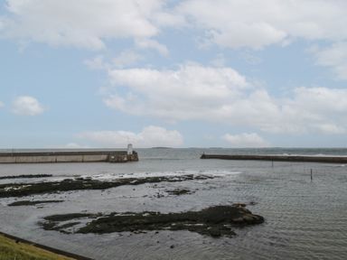 A coastal scene with two stone piers extending into the water and a rocky shoreline at Greenlee House in Seahouses
