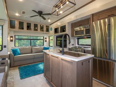 A kitchen and living area with a gray sofa, blue rug, kitchen island with black faucet, stainless steel refrigerator and stove at Tickeydoo, Tor Down Quarry in St Breward