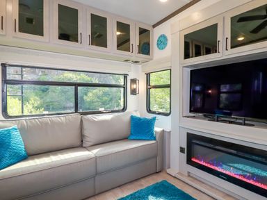 A living area with a grey sofa with blue pillows a television above an electric fireplace and large windows at Tickeydoo Tor Down Quarry in St Breward