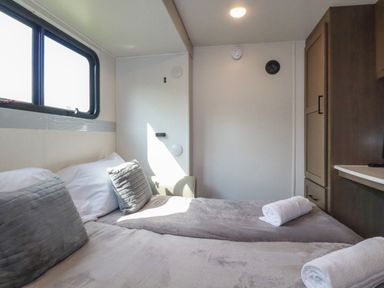 A bedroom with two beds, pillows, rolled towels, a window, and a wooden wardrobe at Tickeydoo, Tor Down Quarry in St Breward