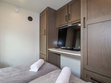 A bedroom with two beds with rolled towels and a television set in built-in wooden cabinetry at Tickeydoo Tor Down Quarry in St Breward