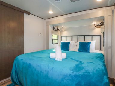 A bedroom with a bed with blue bedspread and pillows and windows on both sides at Tickeydoo Tor Down Quarry in St Breward