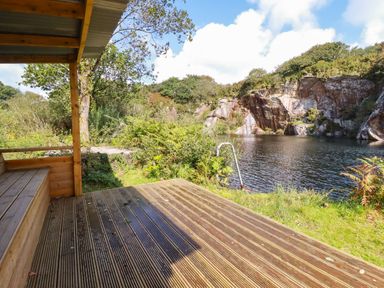 A wooden deck with bench overlooking a quarry lake surrounded by trees and rocks at Tickeydoo Tor Down Quarry in St Breward