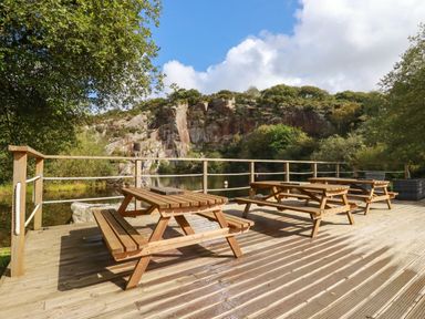 A wooden deck with picnic tables overlooking a quarry lake with rocky cliffs at Tickeydoo Tor Down Quarry in St Breward