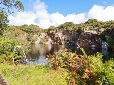 A quarry with water surrounded by rocky cliffs and vegetation at Tickeydoo Tor Down Quarry in St Breward