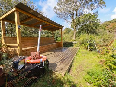 An outdoor wooden seating area with a corrugated metal roof near a grassy path and vegetation at Tickeydoo Tor Down Quarry St Breward