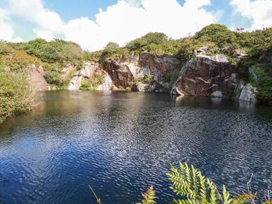 A quarry pond surrounded by rock cliffs and greenery at Tickeydoo Tor Down Quarry in St Breward