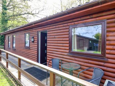 A wooden cabin exterior with windows a door and outdoor table with chairs at The Blacktail in Llanerch Park near St Asaph