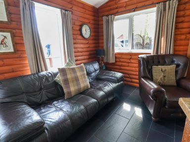 A room with leather sofa and armchair with pillows wooden walls and tiled floor at The Blacktail in Llanerch Park near St Asaph