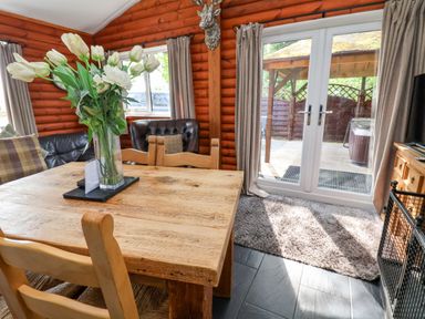 A dining area with a wooden table and chairs a vase of flowers a leather armchair curtains and glass doors at The Blacktail in Llanerch Park near St Asaph