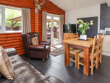 A living area with a leather armchair a wooden dining table with chairs a television and sliding glass doors at The Blacktail Llanerch Park near St Asaph