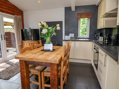 A kitchen and dining area with a wooden table and chairs a vase with flowers a television and cupboards at The Blacktail in Llanerch Park near St Asaph