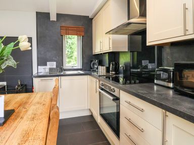 A kitchen with white cabinets a black countertop a wooden dining table and window at The Blacktail in Llanerch Park near St Asaph