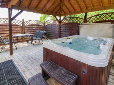 An outdoor covered area with a hot tub table chairs grill and wooden fencing at The Blacktail in Llanerch Park near St Asaph