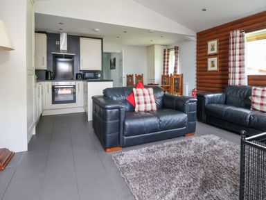 A living room with two black leather sofas a gray rug and an open kitchen area at The Buck in Llanerch Park near St Asaph