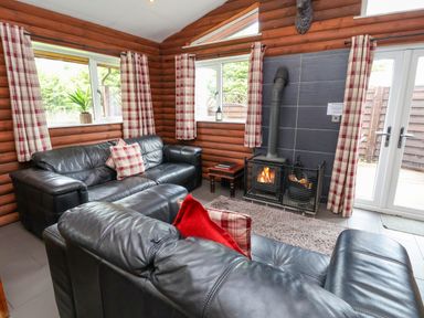 A living room with black leather sofas a fireplace and plaid curtains at The Buck in Llanerch Park near St Asaph