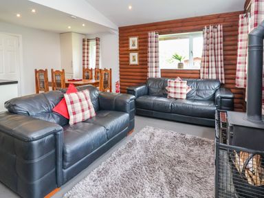 A living room with two black leather sofas and a dining table with wooden chairs at The Buck in Llanerch Park near St Asaph