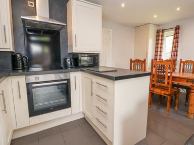 A kitchen with white cabinets oven black countertop and a wooden dining table with chairs at The Buck in Llanerch Park near St Asaph
