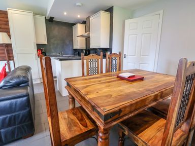A dining area with wooden table and chairs next to a kitchen with white cabinets and black countertop at The Buck in Llanerch Park near St Asaph