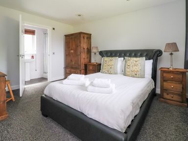 A bedroom with a bed folded towels bedside tables lamps wardrobe and an open door showing a bathroom at The Buck in Llanerch Park near St Asaph