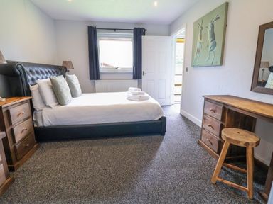 A bedroom with a bed pillows and folded towels a window with curtains wooden nightstands and a wooden dressing table with a stool at The Buck in Llanerch Park near St Asaph