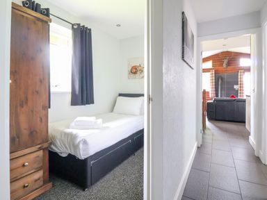 A small bedroom with a single bed and a wooden wardrobe next to a hallway leading to a living room with a mounted deer head at The Buck Llanerch Park near St Asaph