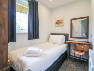 A bedroom with a single bed towels on bed wooden desk mirror and window at The Buck in Llanerch Park near St Asaph