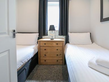 A small bedroom with two single beds separated by a wooden chest of drawers and a lamp on top at The Buck in Llanerch Park near St Asaph