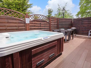 An outdoor patio with a hot tub table chairs a barbecue grill and wooden fencing at The Buck in Llanerch Park near St Asaph