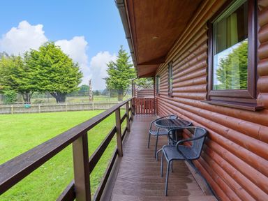 A wooden deck with two chairs and a round table outside a log cabin at The Buck in Llanerch Park near St Asaph