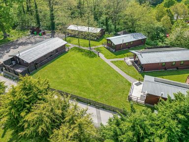 An aerial view of wooden cabins around a grassy area with trees and pathways at The Buck in Llanerch Park near St Asaph
