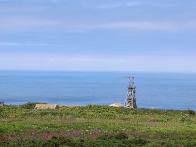 A coastal view with vegetation in the foreground old buildings and a metal structure near the sea at Victory View in Pendeen