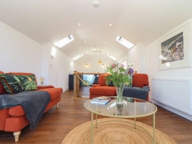 A seating area with two orange sofas, a glass coffee table with flowers, and a framed picture on the wall at Victory View in Pendeen