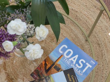 A glass table with a flower vase and books on the coast at Victory View in Pendeen