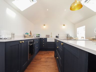 A kitchen with dark cabinets wooden floor a white countertop and gold fixtures at Victory View in Pendeen