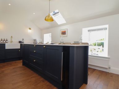A kitchen with dark cabinets a farmhouse sink a kitchen island set with glasses and bowls and wooden flooring at Victory View in Pendeen