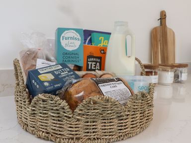 A kitchen countertop with a wicker basket containing milk eggs butter bread biscuits cake and tea at Victory View in Pendeen