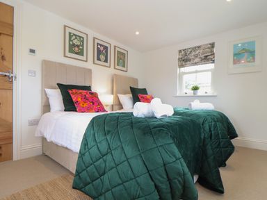 A bedroom with two single beds green quilts pink and green pillows framed artwork and a window at Victory View in Pendeen