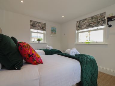 A bedroom with two single beds with green bed runners and rolled white towels under two windows with patterned blinds at Victory View in Pendeen