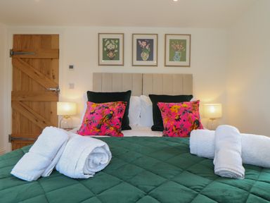 A bedroom with a bed with green quilt and floral cushions with rolled white towels at Victory View in Pendeen