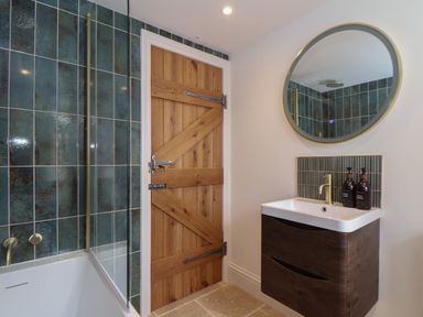 A bathroom with a wooden door a white sink with a round mirror and green tiles at Victory View in Pendeen