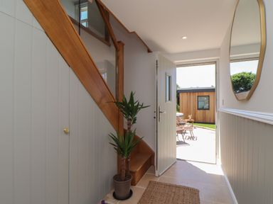 A hallway with a wooden staircase a potted plant a wall mirror an open door leading outside at Victory View in Pendeen