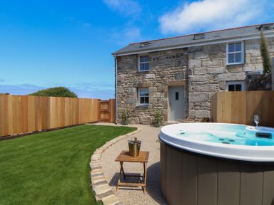A stone house with a wooden fence a hot tub and a small table with drinks in a garden at Victory View in Pendeen